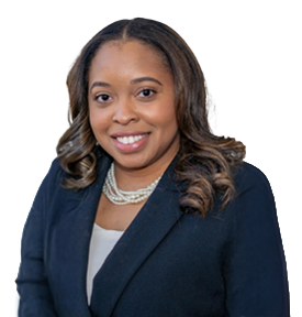 Smiling woman with wavy hair wearing a dark blazer and layered pearl necklaces against a white background.