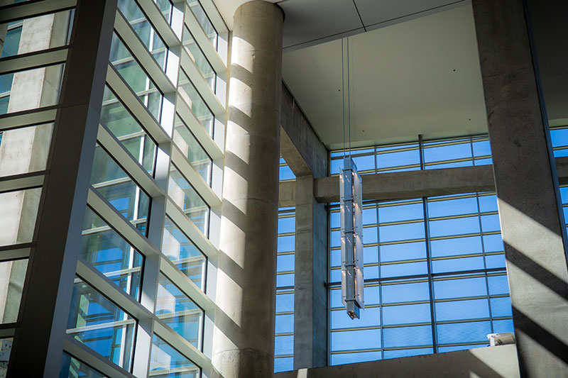 Interior view of a modern building with large grid-patterned windows, concrete columns, and sunlight casting shadows.
