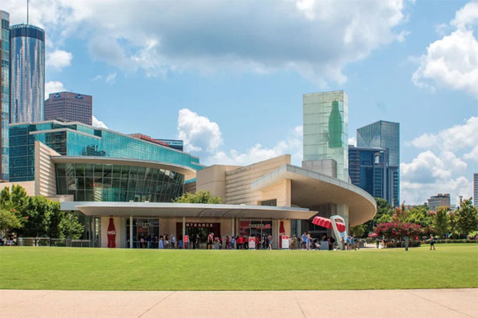 The World of Coca-Cola building with visitors outside, set against a city skyline and partly cloudy sky.