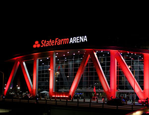 State Farm Arena at night with red illuminated exterior beams and people outside.