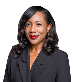 Smiling professional woman with dark curled hair, wearing a black blazer and gold earrings against a gray background.